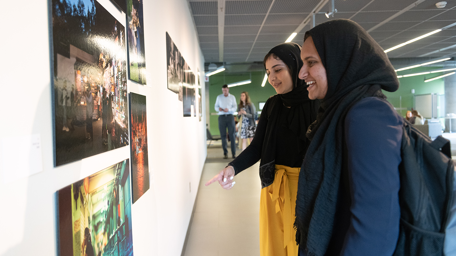 two students wearing hijabs looking at artwork hanging in a gallery and smiling