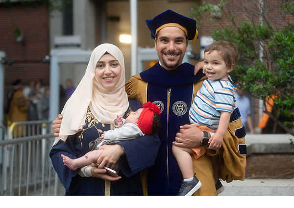 a doctoral graduate poses next to his wife and two children