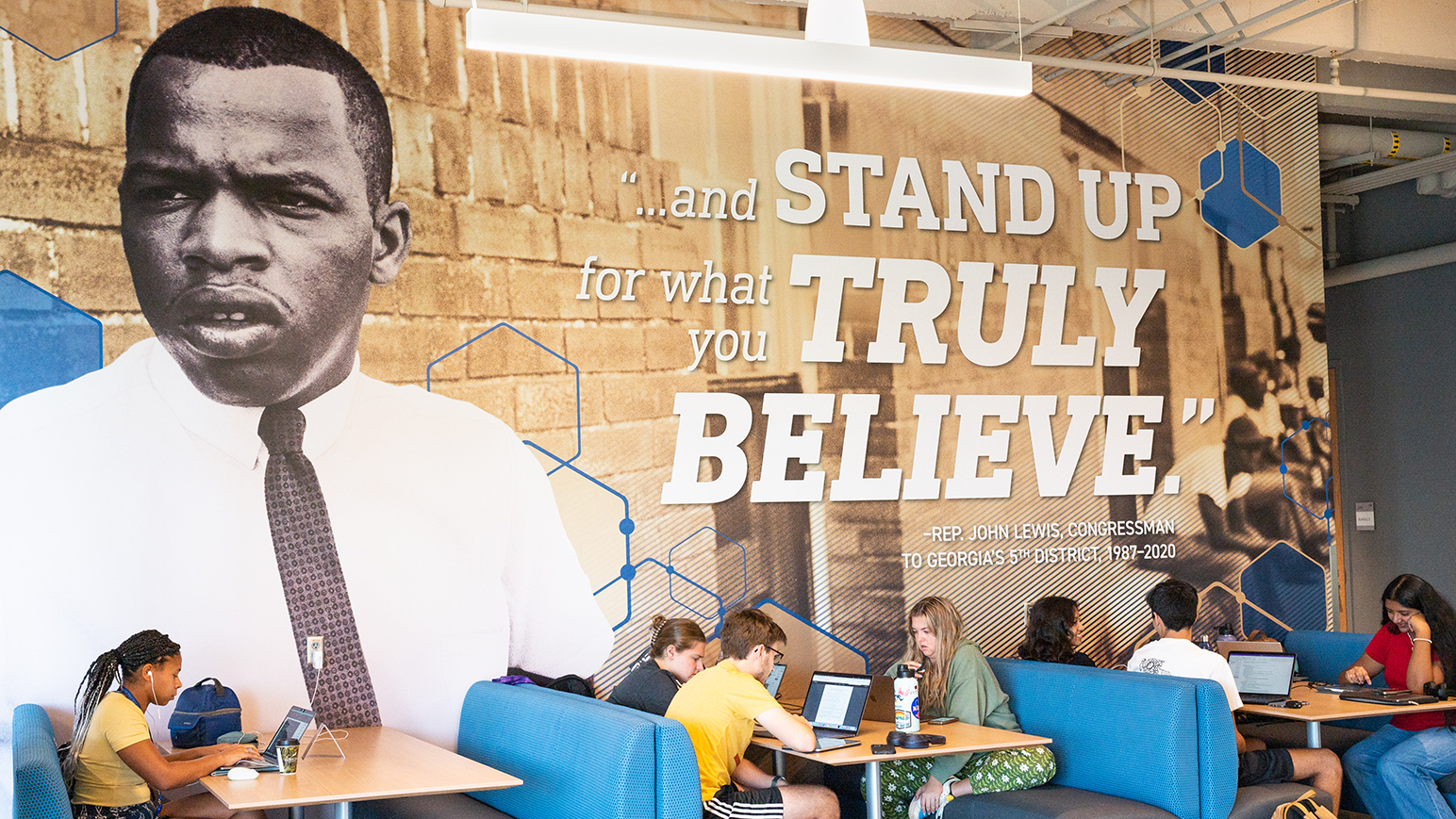 students sit in booths in the student center in front of a mural of John Lewis with text that reads "...and stand up for what you truly believe." - Rep. John Lewis, Congressman to Georgia's 5th district, 1987-2020